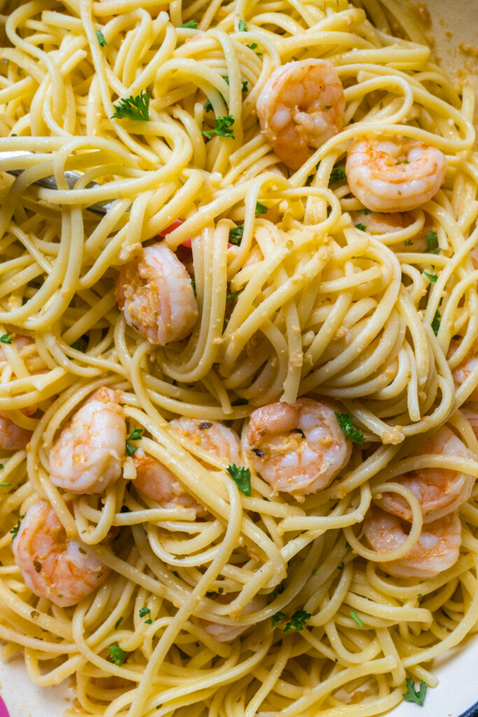 A close-up of cooked linguine pasta mixed with shrimp, garnished with chopped parsley. The dish appears lightly coated with a garlic or olive oil sauce.