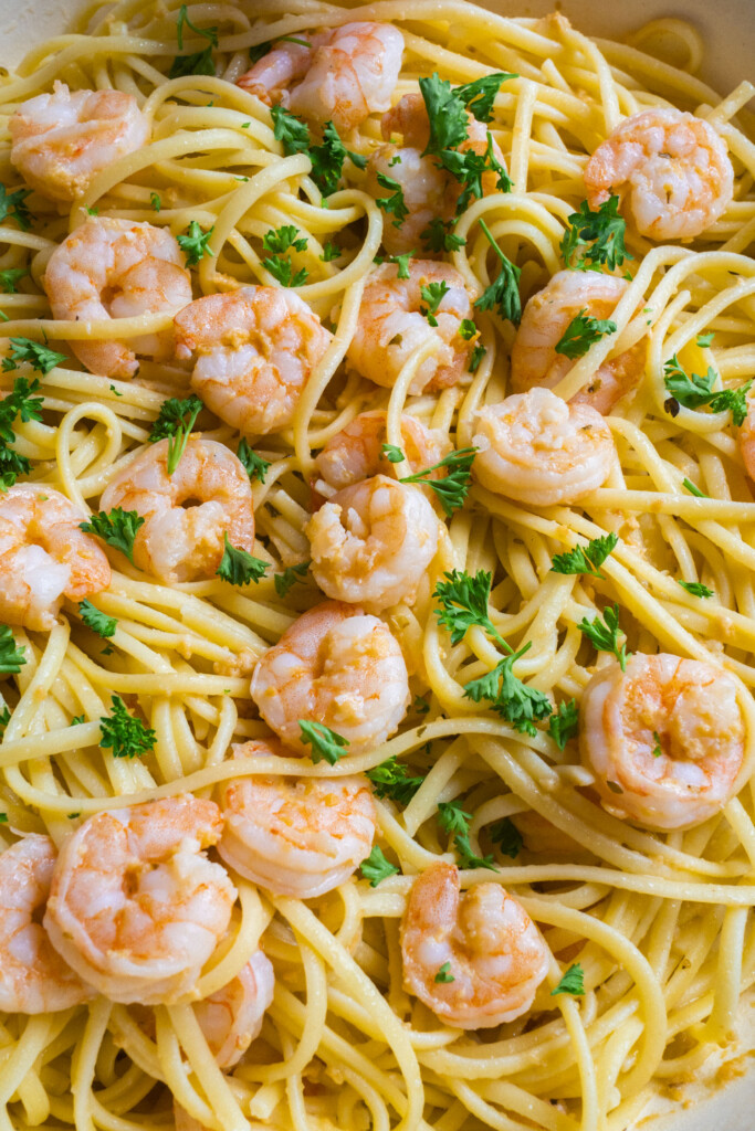 Cooked shrimp and linguine pasta tossed with chopped parsley and a light sauce, served as a close-up shot highlighting the shrimp and fresh herbs scattered over the noodles.