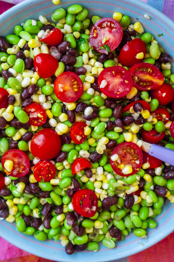 A bowl of salad with cherry tomatoes, corn, black beans, and edamame, mixed together.