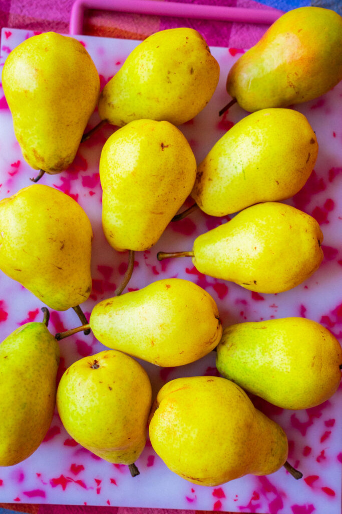 Ten yellow pears arranged on a white cutting board with a pink speckled pattern.