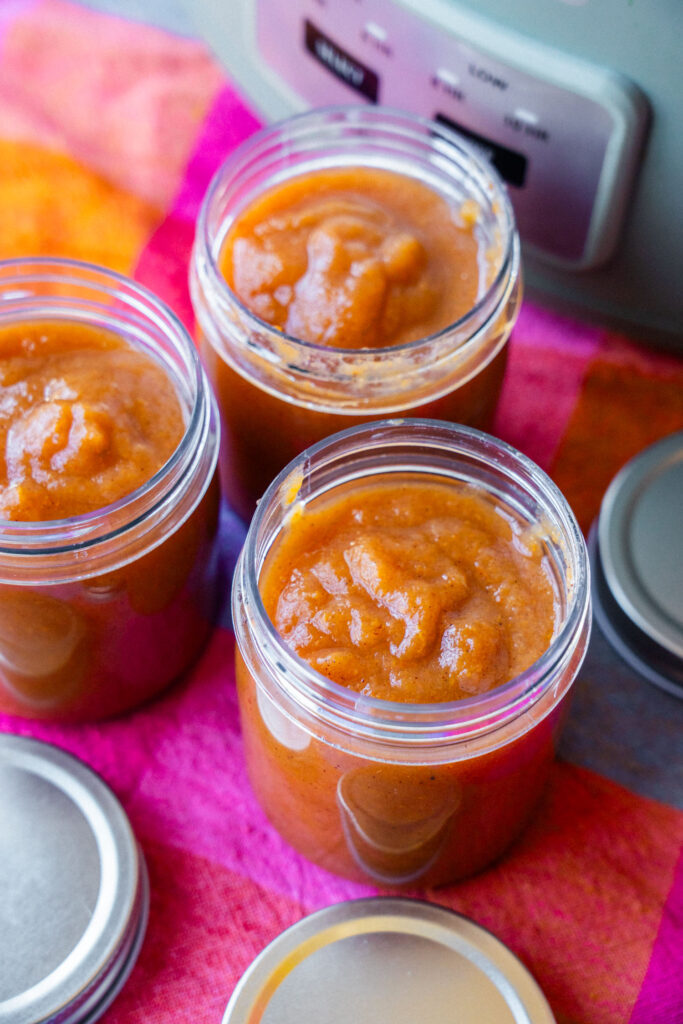 Three open glass jars filled with pear butter on a bright pink and orange cloth.