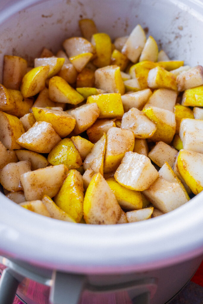 Chopped pears coated in cinnamon inside a slow cooker.