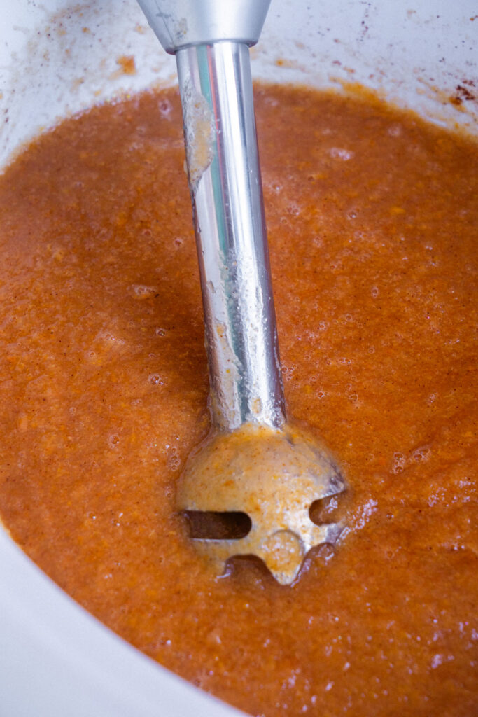 An immersion blender submerged in a bowl of blended pear butter.