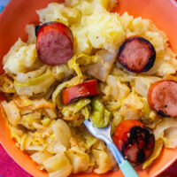 A bowl of mashed potatoes, sautéed cabbage, and sliced seared sausage, with a fork resting in the dish.
