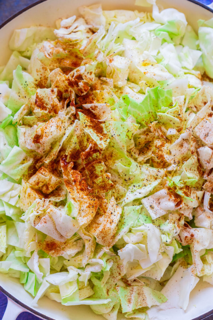 Chopped raw cabbage in a pan, seasoned with a dusting of red and black spices.