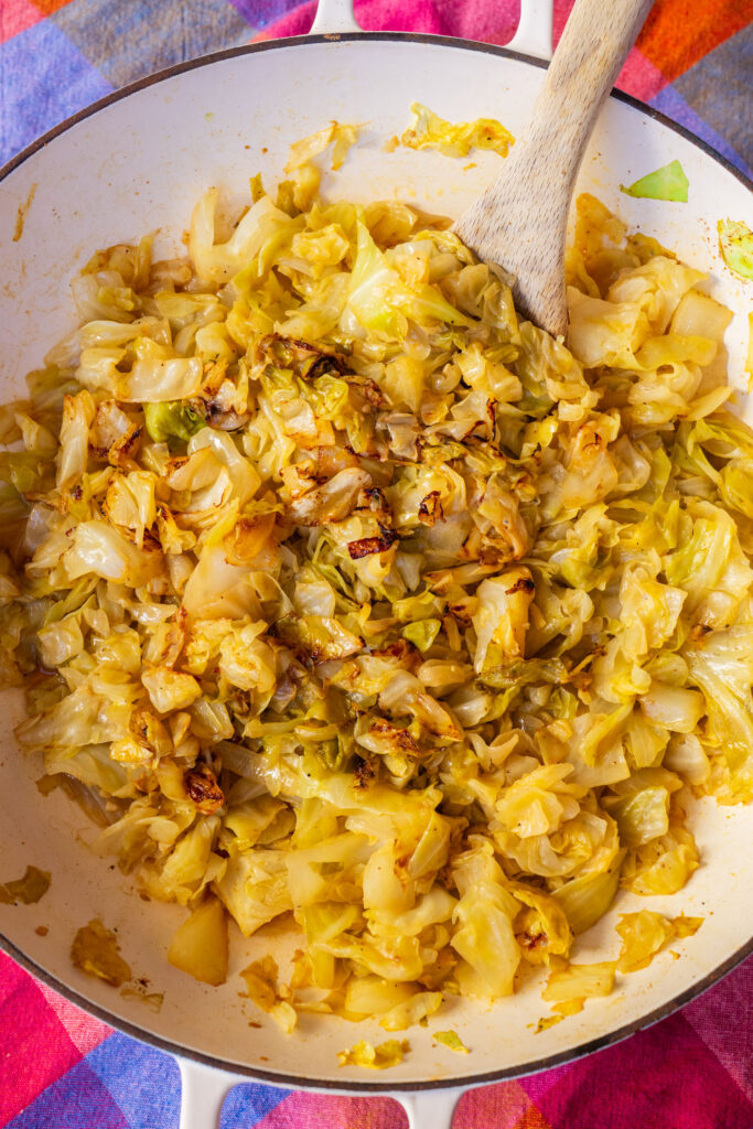 Sautéed cabbage with browned bits in a skillet with a wooden spoon.