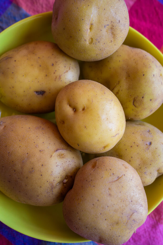 A yellow bowl filled with several raw, unpeeled potatoes.
