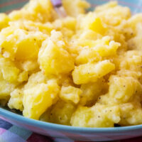 A close-up of a bowl filled with smashed potatoes seasoned with black pepper.