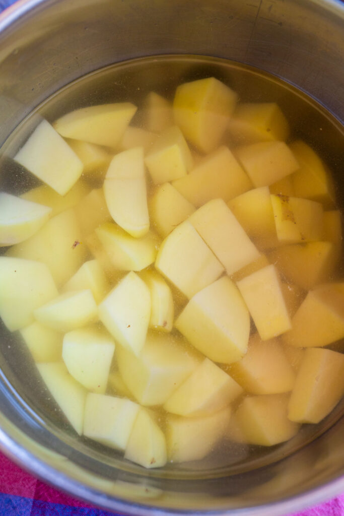 Potatoes peeled and cut into chunks soaking in a pot of water.