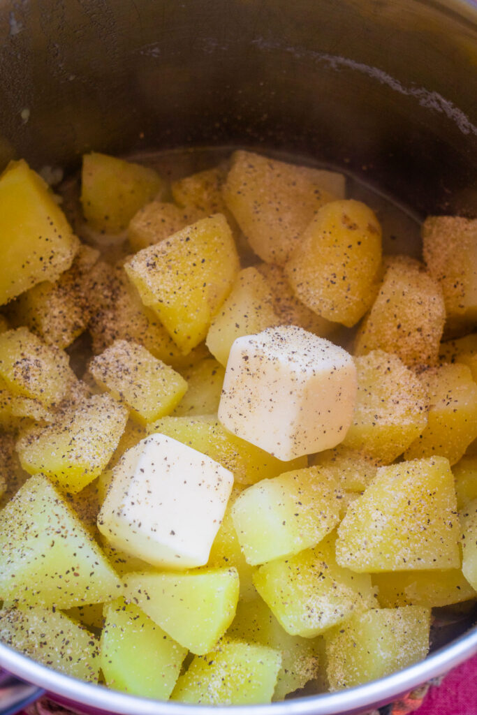 Chunks of boiled potatoes seasoned with pepper and topped with two cubes of butter in a pot.