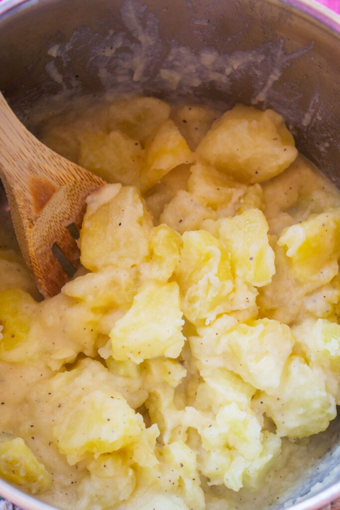 A wooden spoon stirring a pot of cooked, creamy potatoes.